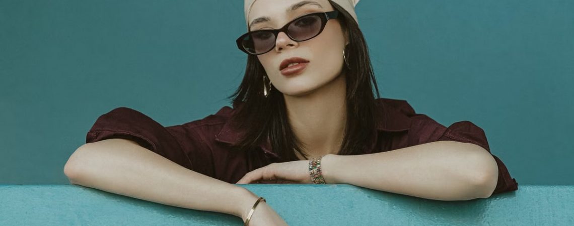 Chic model posing in İstanbul with sunglasses and headscarf against blue backdrop.