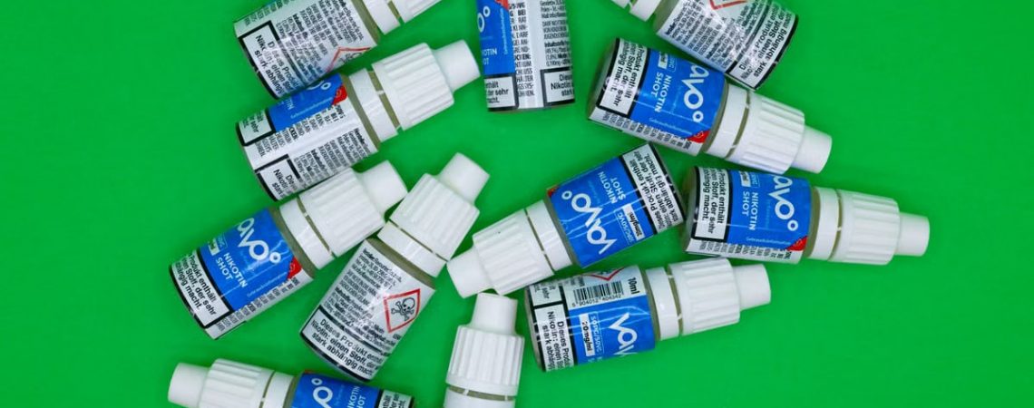 Top view of multiple nicotine vape shot bottles arranged on a green background.